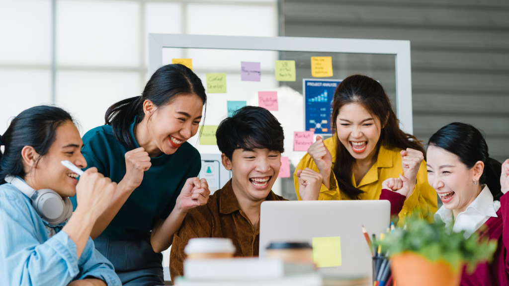 Asian team celebrating a successful KOL Marketing campaign at a laptop in an office.